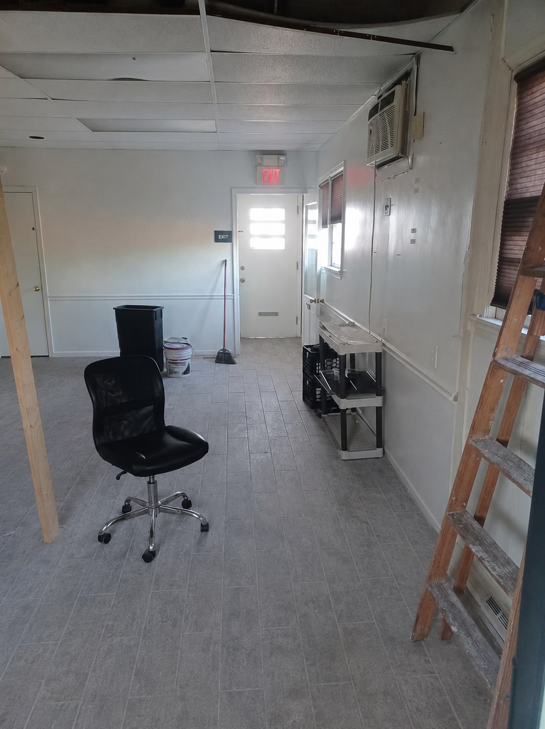 Reverse view of the back room toward the rear exit, windows, wall air conditioner, and open floor area