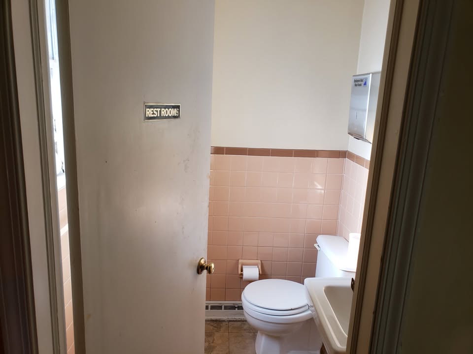 Restroom view with pink wall tile, toilet, sink, and paper towel dispenser